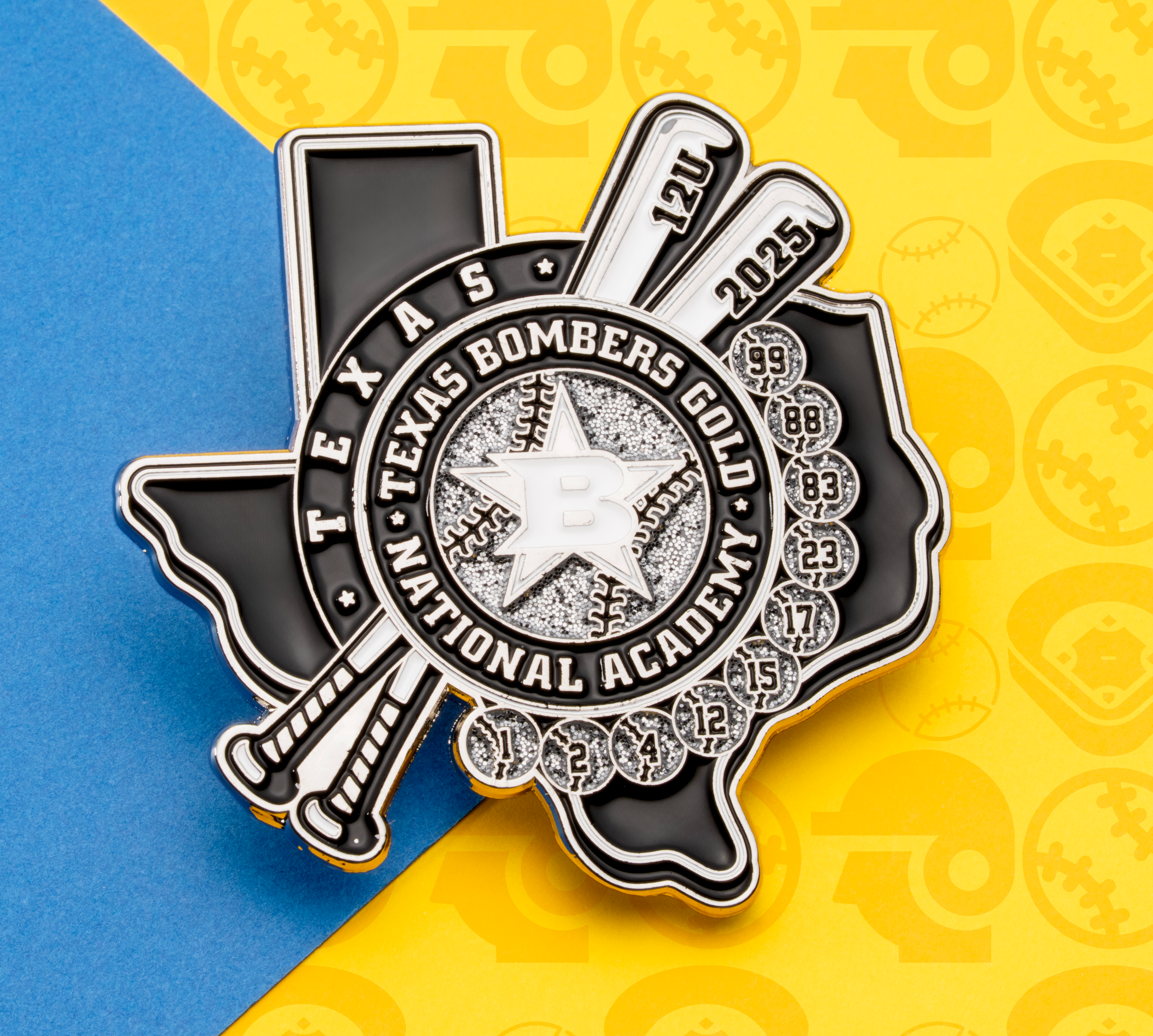 Soft enamel lapel pin in the shape of Texas featuring the Texas Bombers Gold National Academy logo, crossed baseball bats, and glitter accents.